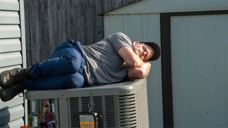 An HVAC technician pretending to sleep on an HVAC outdoor system